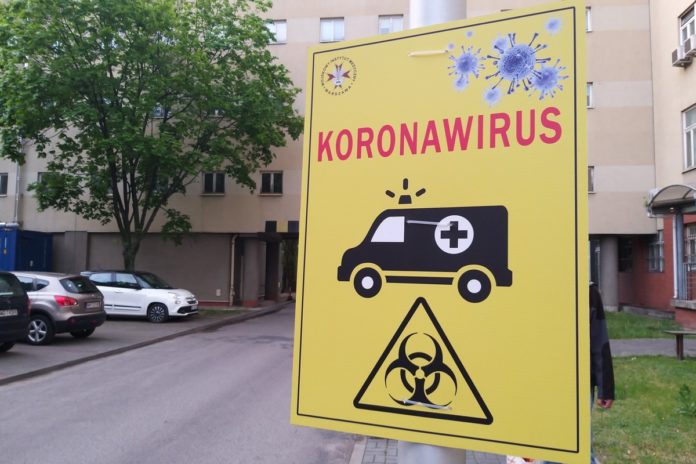 tablica informacyjna, na żółtym tle napis koronawirus, czarny ambulans i znak zagrożenie biologiczne