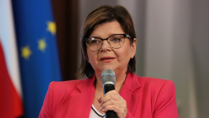 minister zdrowia izabela leszczyna trzyma mikrofon, w tle flagi Polski i Unii Europejskiej