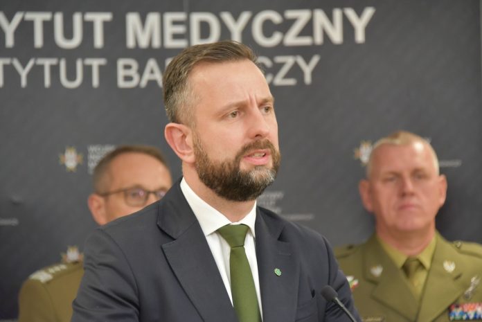 Władysław Kosiniak-Kamysz, wicepremier i minister obrony narodowej przemawia do mikrofonu, w tle banner z napisem Wojskowy Instytut Medyczny